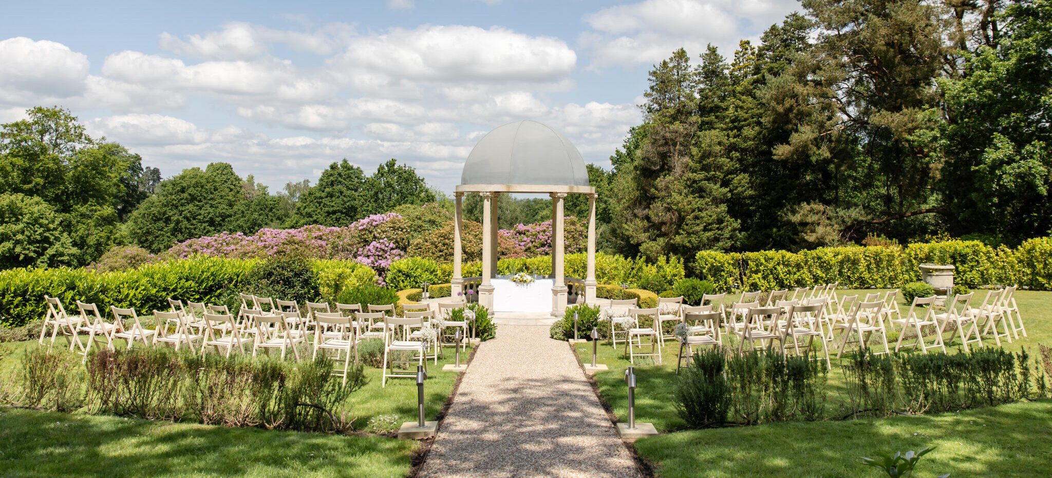 Outdoor country house wedding ceremony set up with rows of chairs facing the garden temple under blue skies at The Spa Hotel, Tunbridge Wells