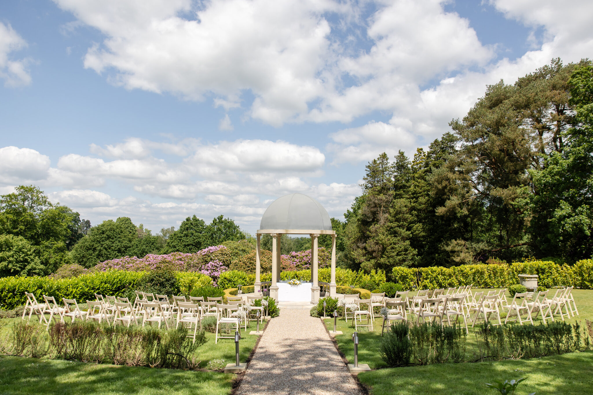 Outdoor country house wedding ceremony set up with rows of chairs facing the garden temple under blue skies at The Spa Hotel, Tunbridge Wells