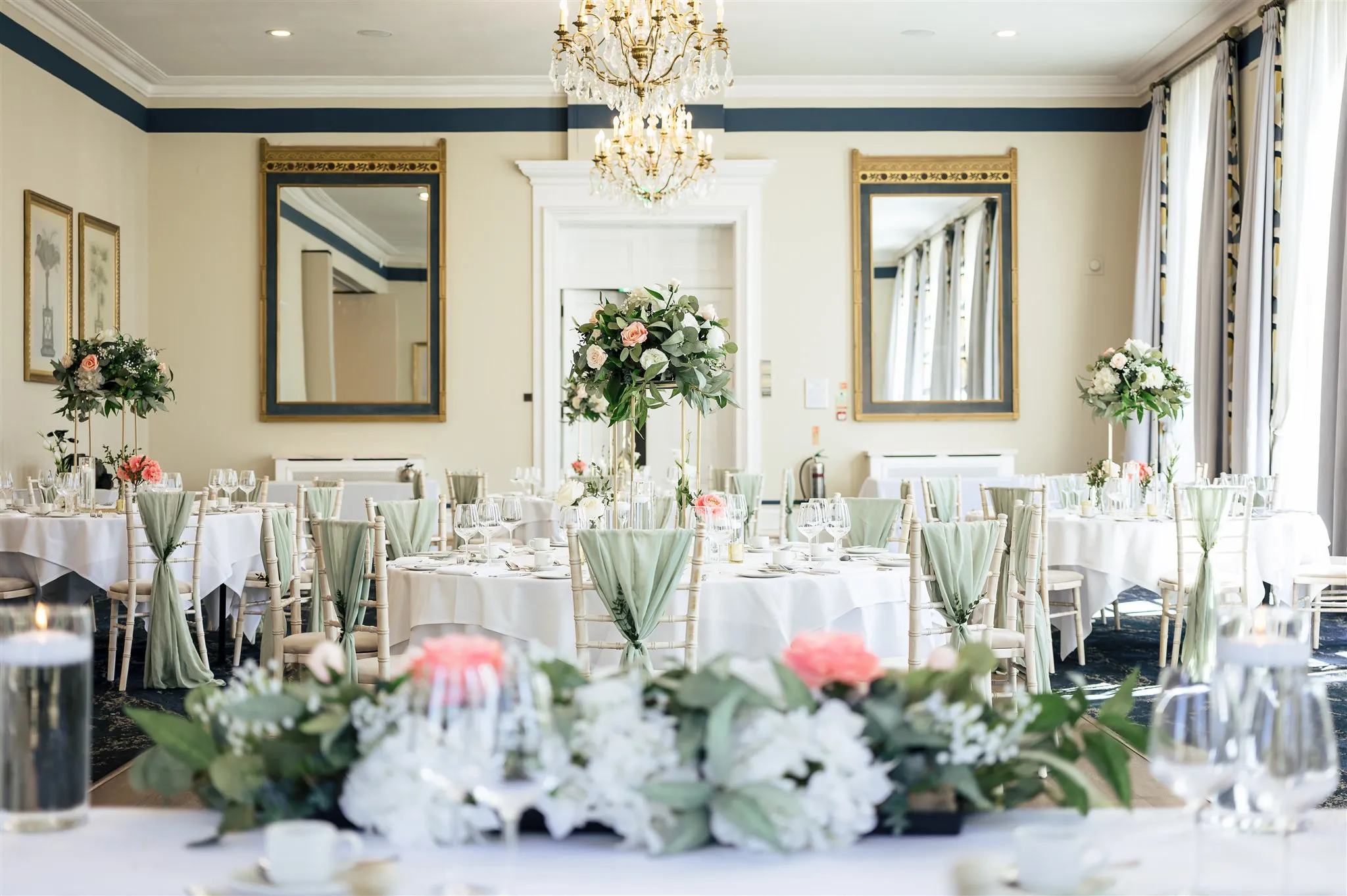The Royal Suite wedding reception tables with sage green chair sashes and tall rose centrepieces on chiavari chairs at The Spa Hotel, Tunbridge Wells